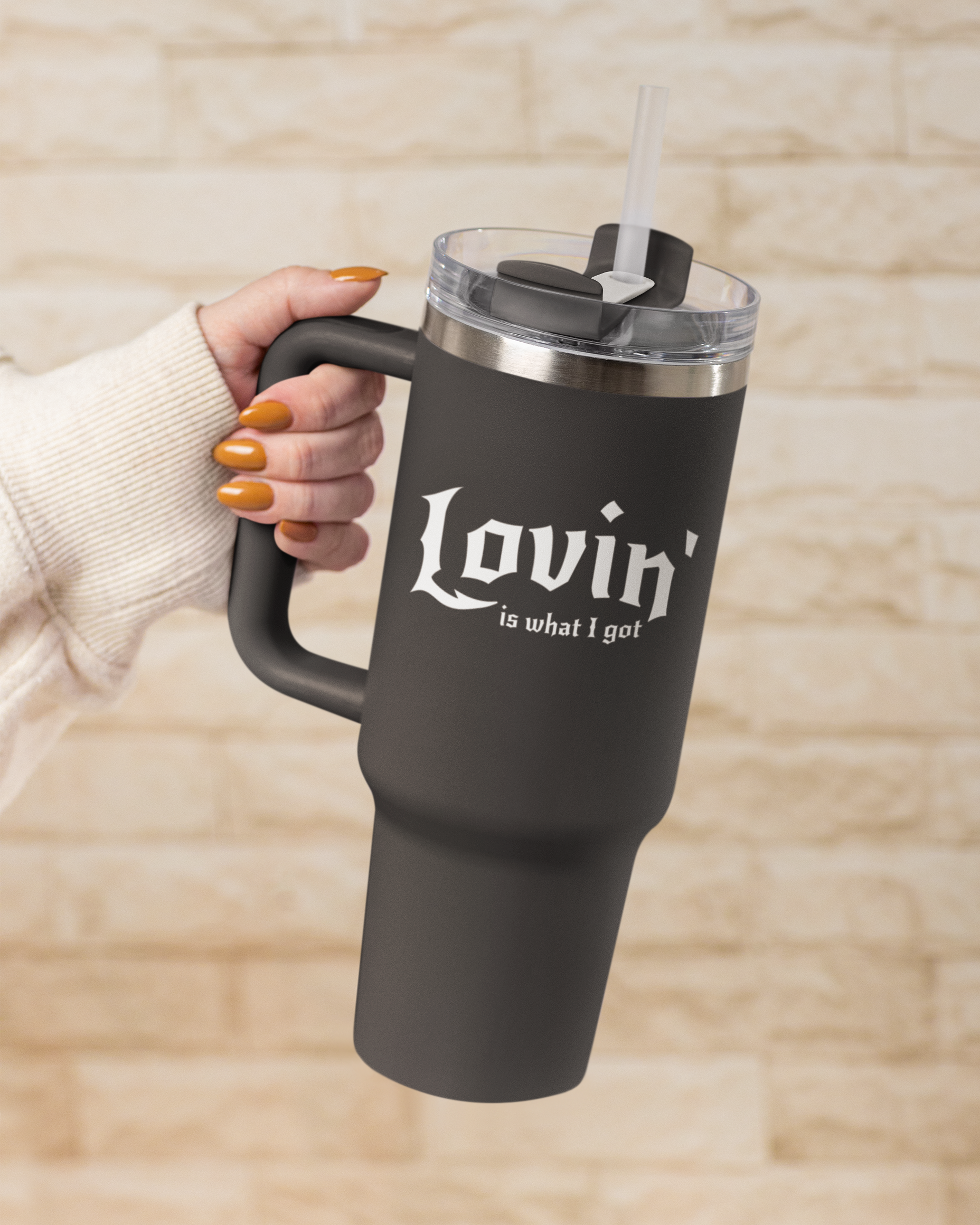 Black travel mug with 'Lovin' is what I got' text held by a person against a beige background