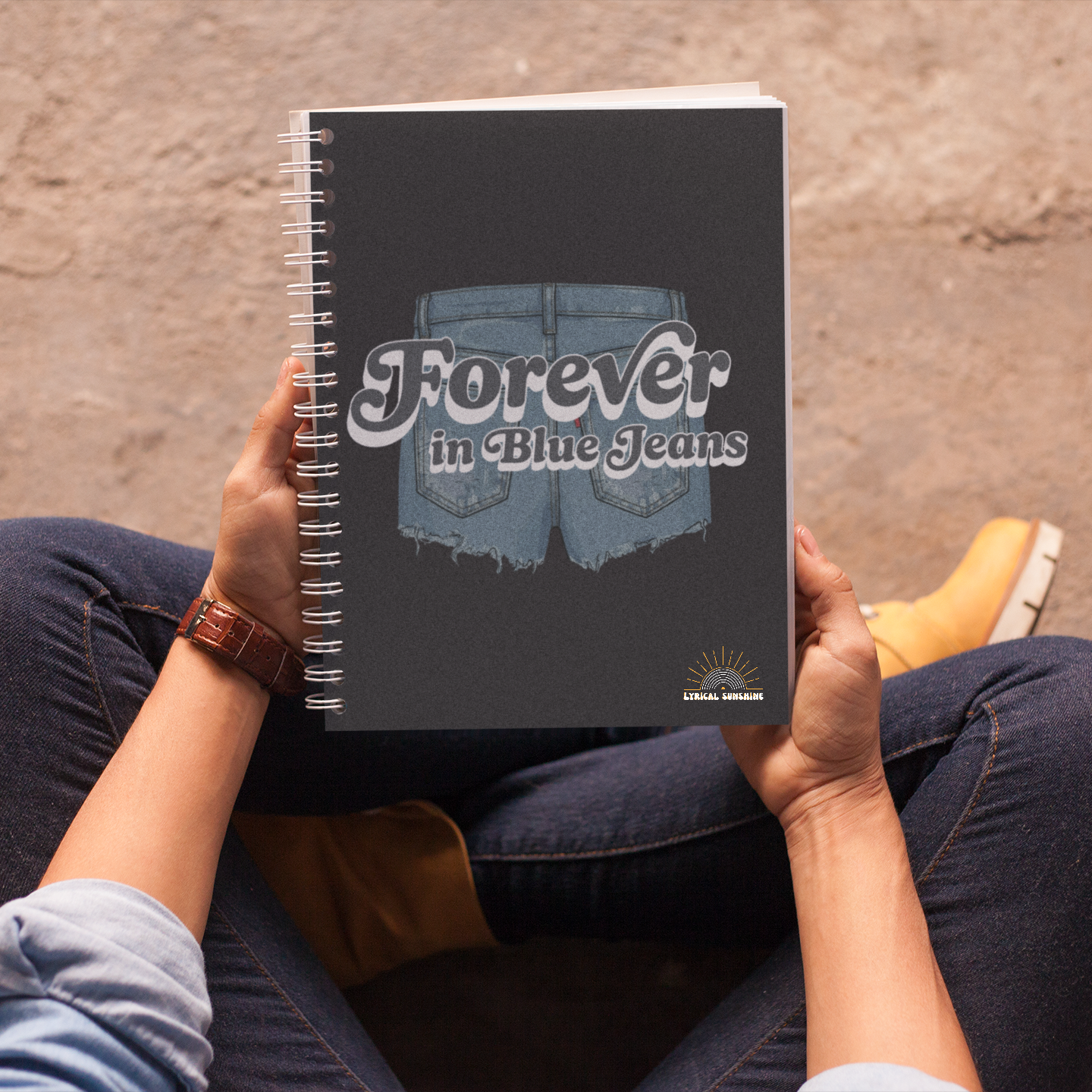 Person holding a notebook with 'Forever in Blue Jeans' design on a textured surface