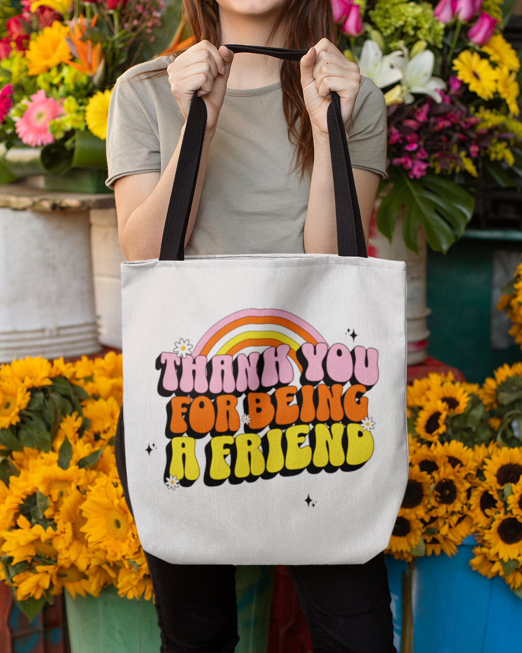 Person holding a tote bag with 'Thank you for being a friend' text in a flower market setting